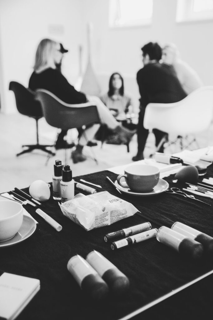 Black and white photo of a group conversation in a fashion studio with makeup tools in foreground.